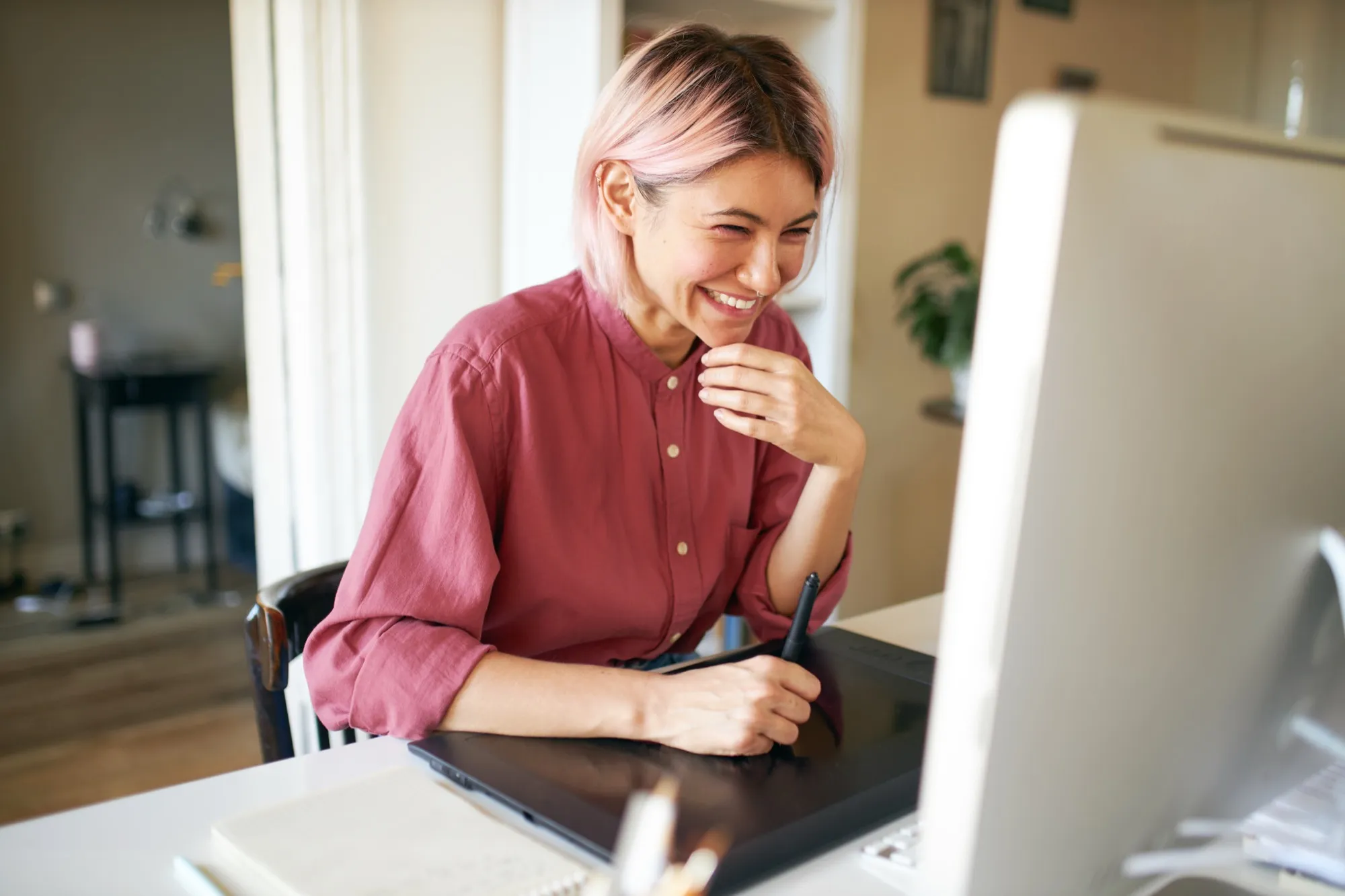 A designer laughing as she works on a drawing tablet at her desk